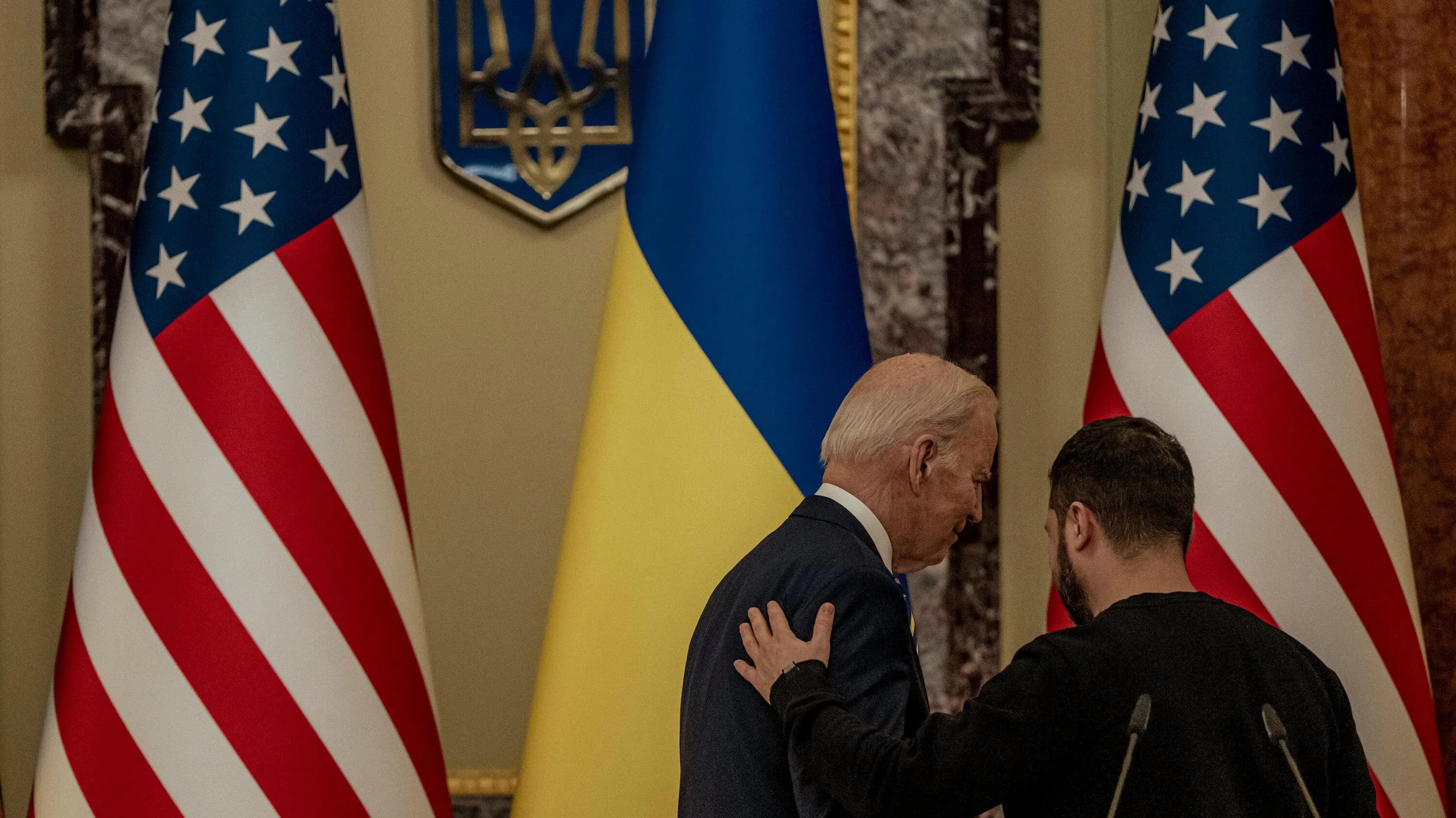 Joe Biden and Volodymyr Zelenskyy engage in a discussion amidst the flags of the United States and Ukraine, signaling a diplomatic dialogue regarding the ongoing conflict in Ukraine.